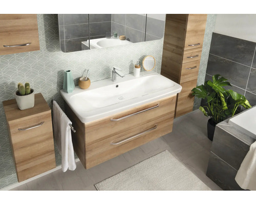 Ensemble de meubles de salle de bains moderne en aspect chêne avec lavabo blanc, armoires assorties, grand miroir et papier peint à motifs.