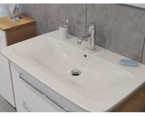 Meuble de salle de bains moderne avec lavabo en céramique blanche et robinet chromé sur un mur de carreaux gris.