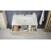 Meuble sous-vasque moderne avec lavabo blanc et tiroir ouvert aspect bois contenant des accessoires de salle de bains.