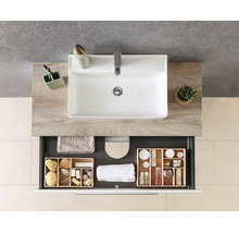 Meuble de salle de bains moderne avec lavabo blanc sur plan de toilette aspect bois et tiroir ouvert avec organiseur en bois et serviettes.