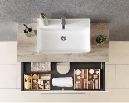 Meuble de salle de bains moderne avec lavabo blanc sur plan de toilette aspect bois et tiroir ouvert avec organiseur en bois et serviettes.