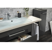 Meuble de lavabo moderne avec vasque en verre, meuble bas anthracite et colonne assortie devant un mur aspect pierre.