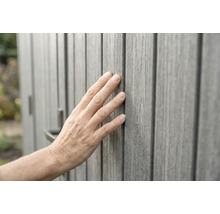 Main touchant un revêtement mural gris aspect bois avec une structure de surface tactile.