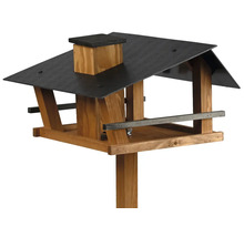 Vogelhaus aus Holz mit dunklem Dach, Schornstein und Pfosten zur Fütterung von Vögeln.