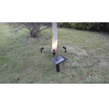 Kit d'éclairage de jardin solaire avec trois spots LED et un panneau solaire dans la pelouse pour éclairer un arbre.