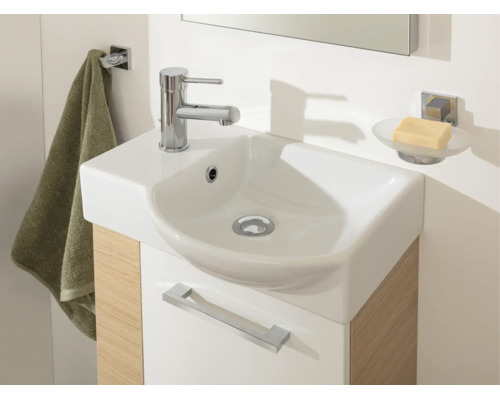 Modernes kleines Waschbecken mit verchromter Armatur auf einem Waschtischunterschrank in Holzoptik mit Handtuchhalter und Seifenschale.