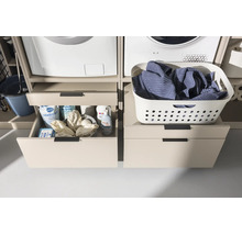 Meuble pour lave-linge avec tiroirs sous le lave-linge et le sèche-linge, ouvert à gauche avec des lessives, fermé à droite avec un panier.