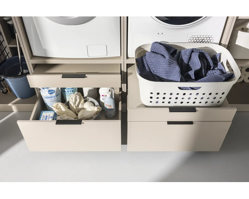 Meuble pour lave-linge avec tiroirs sous le lave-linge et le sèche-linge, ouvert à gauche avec des lessives, fermé à droite avec un panier.