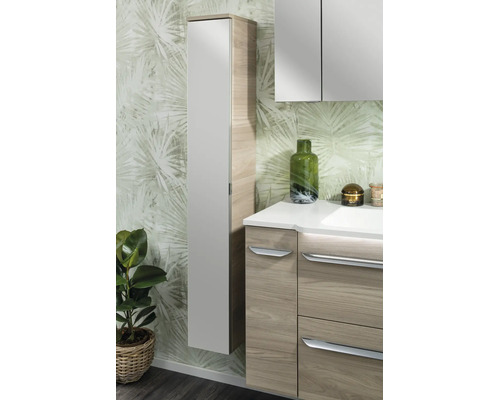 Colonne de salle de bain moderne et meuble sous-vasque aspect bois avec façades claires devant un papier peint à motif de palmes.