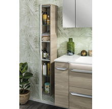 Salle de bain moderne avec armoire haute ouverte aspect bois, meuble sous-lavabo et armoire de toilette devant un papier peint botanique.