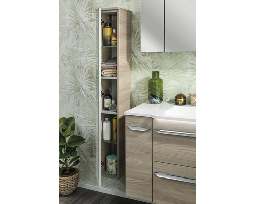 Salle de bain moderne avec armoire haute ouverte aspect bois, meuble sous-lavabo et armoire de toilette devant un papier peint botanique.