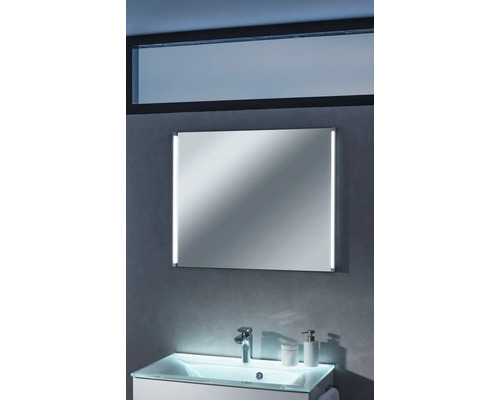 Miroir de salle de bain rectangulaire avec éclairage LED latéral, monté au-dessus d'un meuble sous-vasque sur un mur gris.