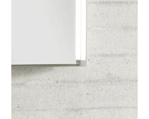 Gros plan sur le coin d'un miroir avec cadre métallique et éclairage latéral à LED intégré sur un mur texturé.