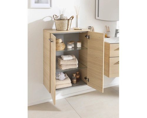 Armoire de salle de bain murale en aspect bois clair avec deux portes, trois étagères en verre et des articles de toilette bien rangés.