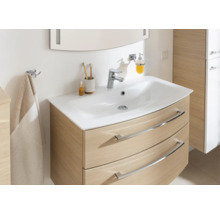 Meuble de salle de bains moderne avec meuble sous-vasque incurvé aspect chêne, vasque blanche, robinet chromé et accessoires.