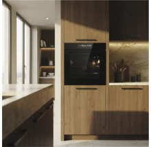 Cuisine moderne avec un four noir encastré dans des meubles en bois, une paroi arrière en marbre et une atmosphère lumineuse.