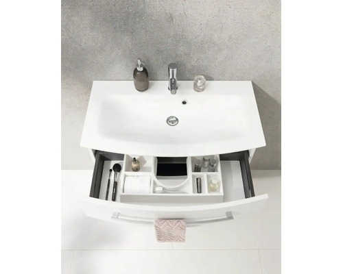Lavabo blanc avec robinetterie et meuble sous-lavabo avec tiroir ouvert comprenant un système de rangement et des articles de toilette.