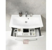 Lavabo blanc avec robinetterie et meuble sous-lavabo avec tiroir ouvert comprenant un système de rangement et des articles de toilette.