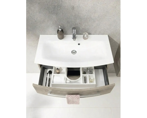 Salle de bain lumineuse et organisée avec meuble sous-vasque moderne, vasque en céramique blanche et tiroir ouvert avec système de rangement.