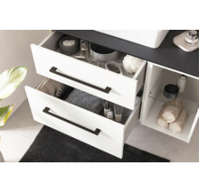 Meuble sous-vasque blanc avec deux tiroirs ouverts, poignées noires, compartiment ouvert avec tablette en verre et plan de travail foncé.