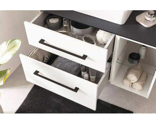 Meuble sous-vasque blanc avec deux tiroirs ouverts, poignées noires, compartiment ouvert avec tablette en verre et plan de travail foncé.