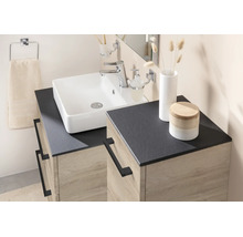 Salle de bain moderne avec vasque à poser blanche, plan de travail sombre et meuble sous-vasque aspect chêne avec poignées noires.