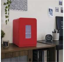 Roter Mini-Kühlschrank mit Sichtfenster auf einem Holzschrank in einem hellen, organisierten Raum mit Bürozubehör.