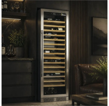 Hoher Weinkühlschrank mit Edelstahlrahmen und Glastür, eingebaut in eine Wand neben einem Ledersessel in einem modern gestalteten Wohnraum.