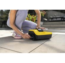 Person montiert Bürstenwalze an einem Kärcher Terrassenreiniger auf einer Steinterrasse.