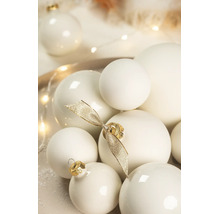 Verschiedene cremeweisse Weihnachtskugeln in matter und glänzender Optik, dekoriert mit einer goldenen Schleife.