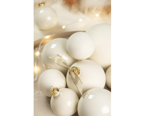 Verschiedene cremeweisse Weihnachtskugeln in matter und glänzender Optik, dekoriert mit einer goldenen Schleife.