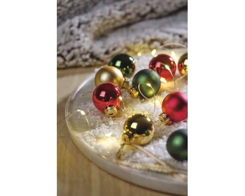 Festliches Arrangement aus Weihnachtskugeln in Rot, Grün und Gold auf einem Tablett mit Kunstschnee und LED-Lichterkette.