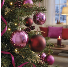 Geschmückter Weihnachtsbaum mit glänzenden und matten Christbaumkugeln, Beeren und Bändern in einem gemütlichen, hellen Wohnzimmer.