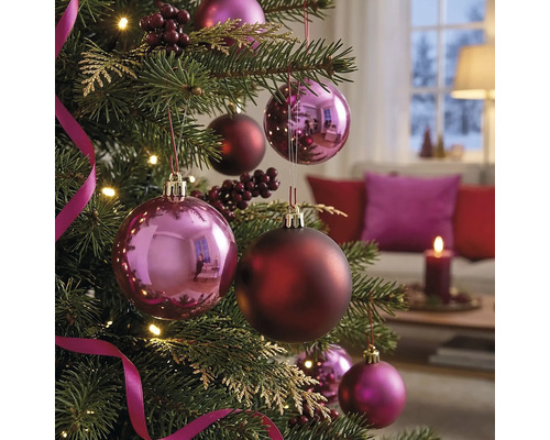 Geschmückter Weihnachtsbaum mit glänzenden und matten Christbaumkugeln, Beeren und Bändern in einem gemütlichen, hellen Wohnzimmer.
