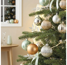 Weihnachtsbaum geschmückt mit matten, glänzenden und geriffelten Kugeln, silbernen Dekoblättern und einer Lichterkette in einem hellen Zimmer.