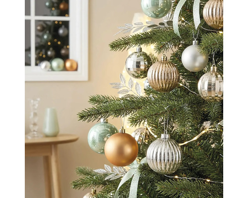 Weihnachtsbaum geschmückt mit matten, glänzenden und geriffelten Kugeln, silbernen Dekoblättern und einer Lichterkette in einem hellen Zimmer.
