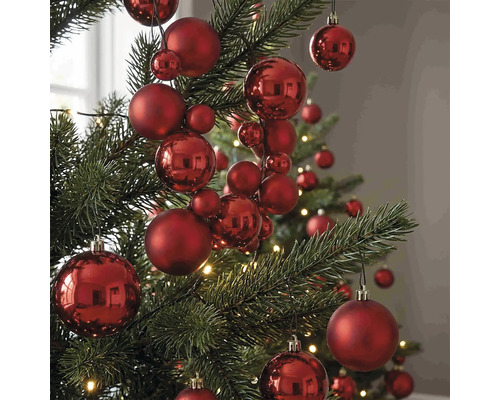 Rote Christbaumkugeln in verschiedenen Größen mit matter und glänzender Oberfläche an einem Weihnachtsbaum.