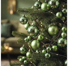 Grüne Weihnachtskugeln in verschiedenen Größen, teils glänzend, teils matt, an einem Weihnachtsbaum mit Lichterkette.