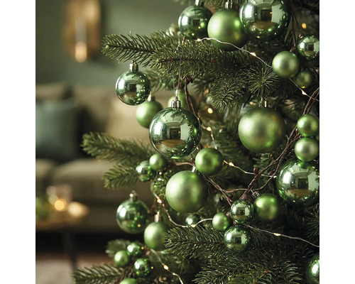 Grüne Weihnachtskugeln in verschiedenen Größen, teils glänzend, teils matt, an einem Weihnachtsbaum mit Lichterkette.