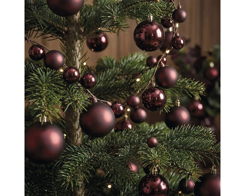 Weihnachtsbaum mit dunkelroten Christbaumkugeln in verschiedenen Grössen, matt und glänzend, mit einer Kugelgirlande und Lichtern dekoriert.