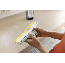 Mains tenant un suceur pour lave-vitres Kärcher au-dessus d'un plan de travail.