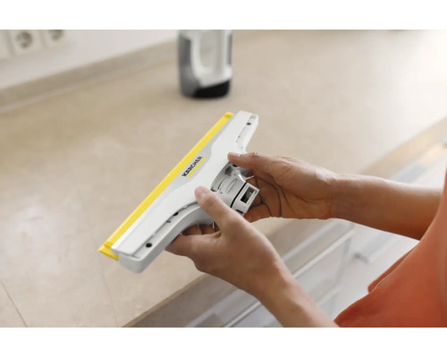 Mains tenant un suceur pour lave-vitres Kärcher au-dessus d'un plan de travail.