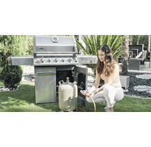Une femme branche une bouteille de gaz sur un barbecue à gaz Napoleon en acier inoxydable dans un jardin lumineux et organisé.