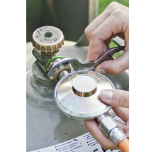 Une personne utilise une clé pour bouteille de gaz CFH pour raccorder un détendeur de gaz à une valve de bouteille de gaz.