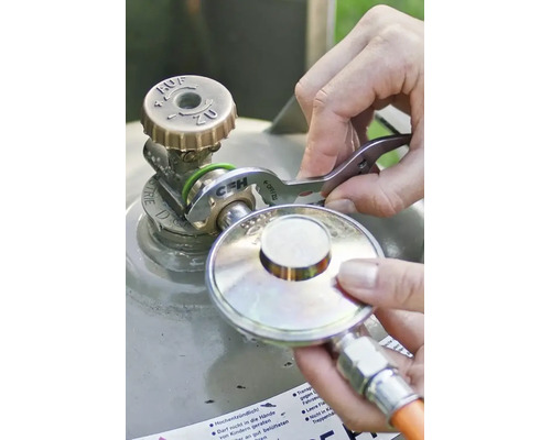 Une personne utilise une clé pour bouteille de gaz CFH pour raccorder un détendeur de gaz à une valve de bouteille de gaz.