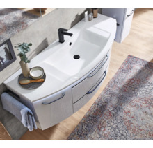 Meuble sous-vasque blanc moderne avec mitigeur noir, rangement courbé et accessoires de salle de bain sur parquet clair avec tapis à motifs.