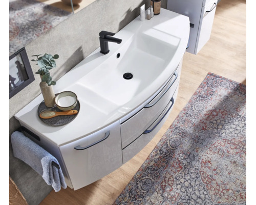 Meuble sous-vasque blanc moderne avec mitigeur noir, rangement courbé et accessoires de salle de bain sur parquet clair avec tapis à motifs.