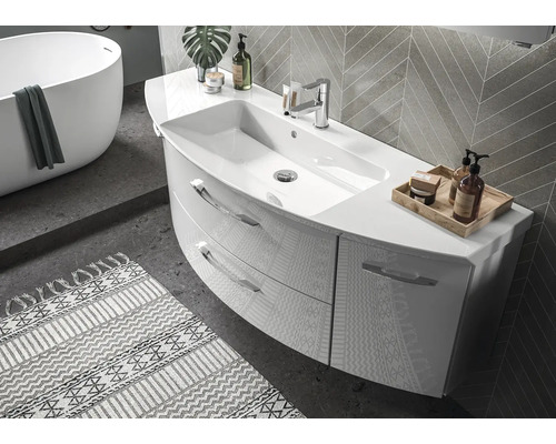 Salle de bains moderne avec meuble incurvé, deux tiroirs et robinetterie. Baignoire îlot et carrelage mural en arrière-plan.