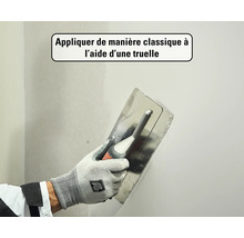 Main avec gant de travail appliquant de l'enduit sur un mur à l'aide d'une lisseuse.