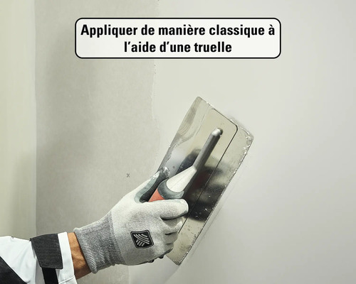 Main avec gant de travail appliquant de l'enduit sur un mur à l'aide d'une lisseuse.